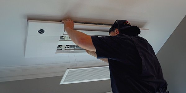 Technician installing a ceiling-mounted ductless mini-split indoor unit
